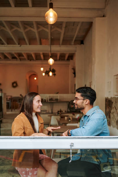 Smiling young man and woman talking together in a cafe during a date Young man and woman talking and smiling while sitting by a cafe window during a first date together blind date stock pictures, royalty-free photos & images