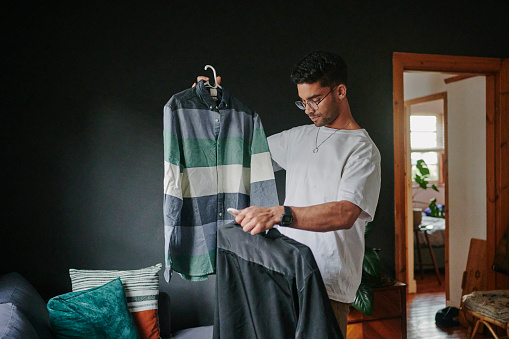 Young man looking at different shirt while trying to choose an outfit at home before for a date