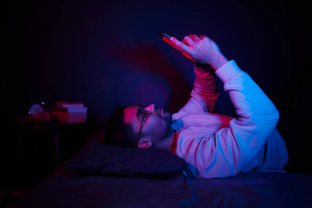 Smiling young man texting on his phone on his bed at night
