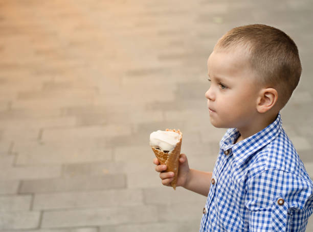 istock The boy eats ice cream. A beautiful, Caucasian, fair-haired boy, 4 years old, cheerfully and emotionally licks ice cream in a waffle cup with his tongue on the street in summer. Close-up. 1555735049