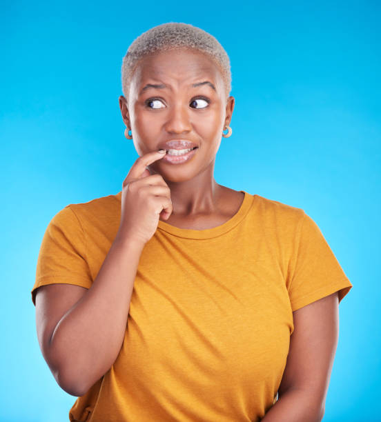 istock Black woman, biting nails and anxiety in studio with thinking, confused or ideas for decision by blue background. African girl, stress and finger in mouth for fear, scared or brainstorming for choice 1555735605
