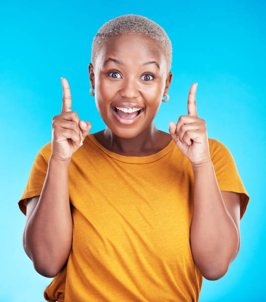 istock Excited portrait, pointing up and happy black woman gesture at eureka, problem solving solution or ideas. Wow, OMG notification and African person smile for studio realisation on blue background 1555736140