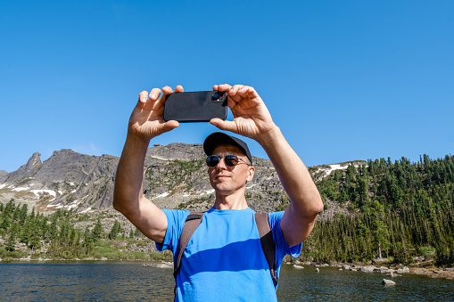 Traveling man using phone to take a photoes in mountain landscape. Blogger take a selfie