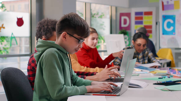 istock Teenage male student sit at desk and write task in notebook using laptop 1555753610