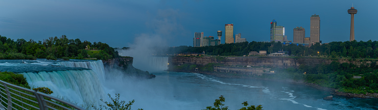 Niagara Falls, NY and Canada water falls and viewing areas with buildings and cityscape seen in Canada across river in the early morning light