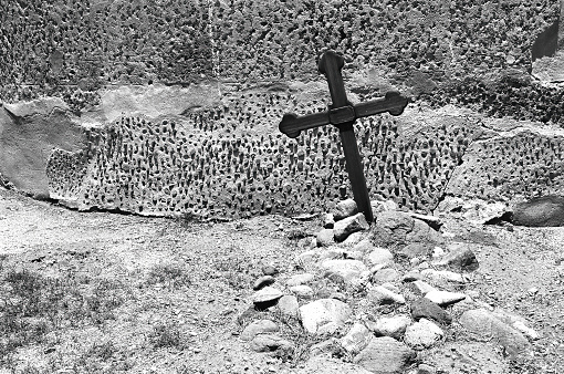 A low angle of a stone cross on a pedestal against green trees at golden hour