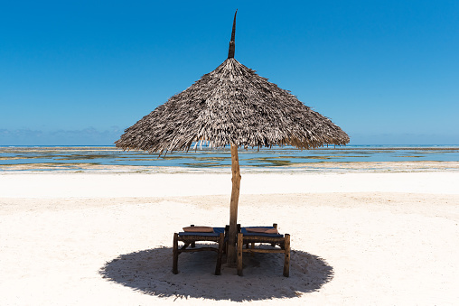Lonely wooden umbrella on a beach of the Indian Ocean, blue sky et sunny tropical weather, Zanzibar, Tanzania