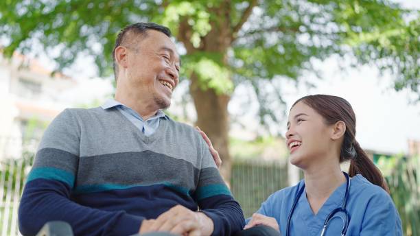 une infirmière soignante asiatique encourage un patient âgé assis dans un fauteuil roulant. l’infirmière soignante prend soin et soutient le patient âgé de sexe masculin - patient male nurse nurse hospital photos et images de collection