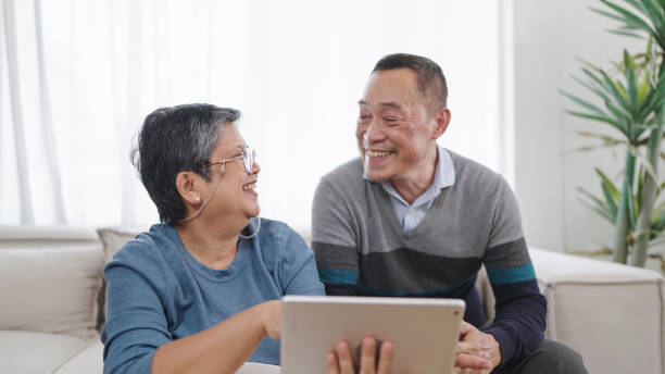 istock Happy elderly asian couple talking together and using tablet enjoy browsing social media while sitting in living room at home. Elderly couple love moment. Couple retirement lifestyle 1555815336