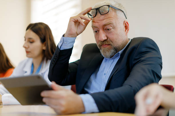 istock Navigating Vision Challenges: Mature Businessman Struggling to Read Tablet During Conference 1555822173