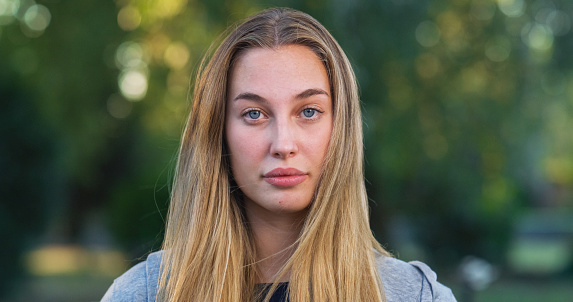 Close Up Portrait of Beautiful Young Woman Looking at Camera Neuterally with a Greenery Background. Blond Female Teenager Enjoying Fresh Air in the Park and Taking Care of her Wellbeing