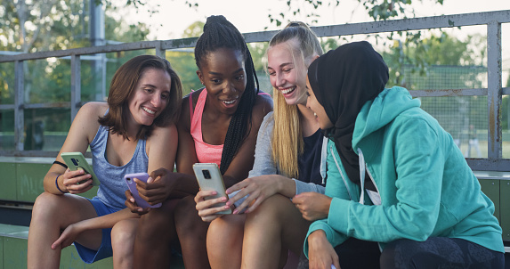 Group of Young Multiethnic Female Teenagers Sitting in a Public Park and Watching a Funny Video on Smartphones. Group of Friends Having Fun Together Outdoors While Staying Connected