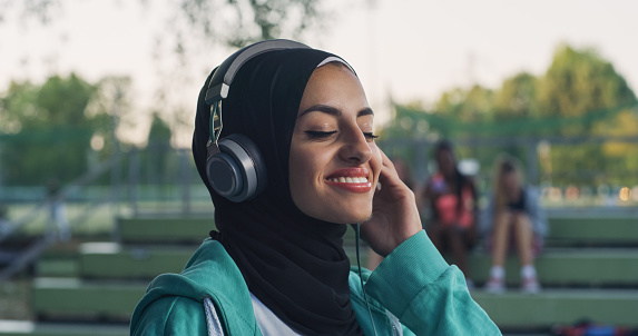 Closeup Portrait of Beautiful Arab Woman Smiling While Putting on her Headphones in the Park During her Early Morning Walk. Female Teenager Enjoying Music and Fresh Air While Being Outdoors
