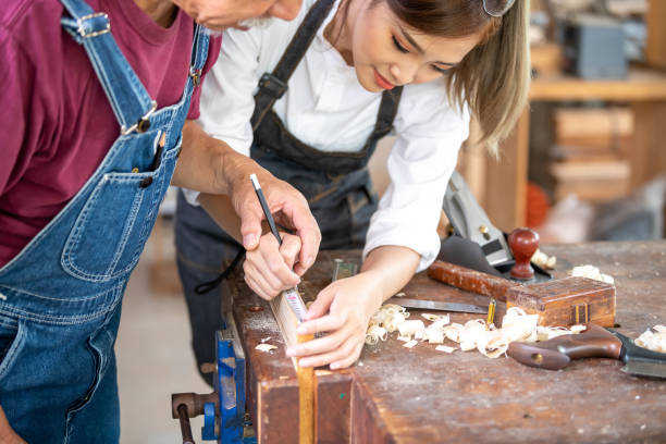 istock Crop unrecognizable craftswoman making marks on wooden detail while working with anonymous colleague in carpentry workshop 1555859769