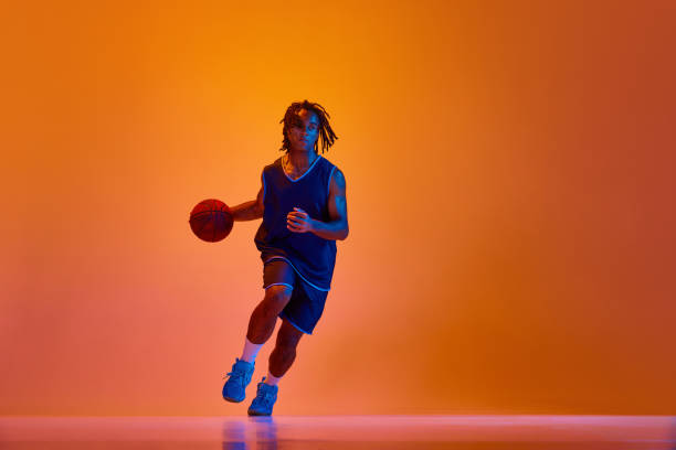 istock Young athletic man, basketball player in motion during game, training against orange background in neon lights 1555861496