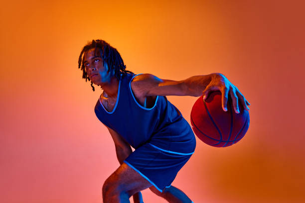 istock Young athletic man, basketball player in motion during game, training against orange background in neon lights 1555861948