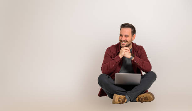 istock Smiling handsome male entrepreneur with hands clasped looking away while sitting with crossed legs. Young sales executive working over wireless computer and posing cheerfully on background 1555862019