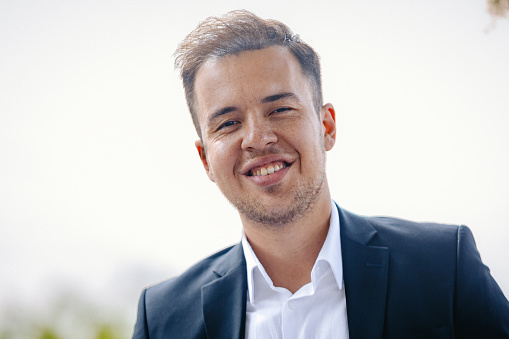 Close-up head and shoulders portrait of cheerful young businessman smiling and posing for a close-up portrait looking at the camera and smiling charmingly. standing in office on gray background with copy space area xxxl