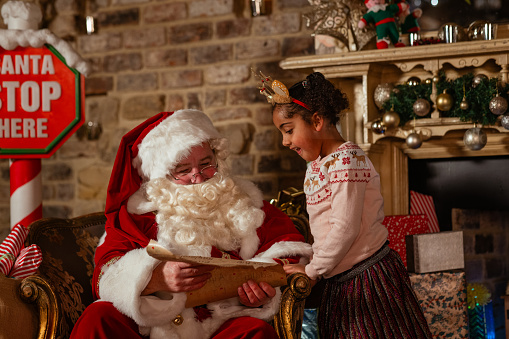 Girl visiting Santa at a Santas grotto in Newcastle Upon Tyne. Santa is reading a 'naughty or nice' list with her.