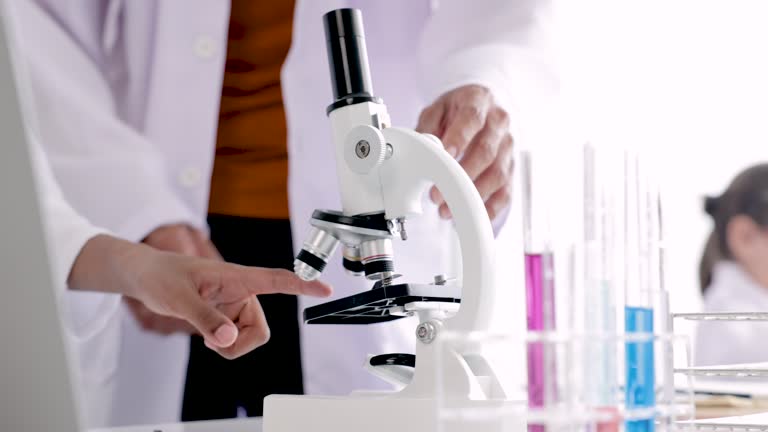 Kindness Hispanic teacher with beard and student in class, African boy focus with microscope for experimental result, teacher pay attention to schoolkids, science education in classroom concept