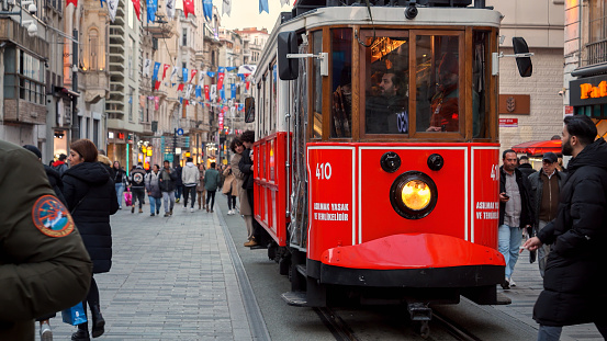 Famous Istanbul red tram driving on the crowded Istiklal street at sunset. 15th of March, 2023, Turkey, Istanbul