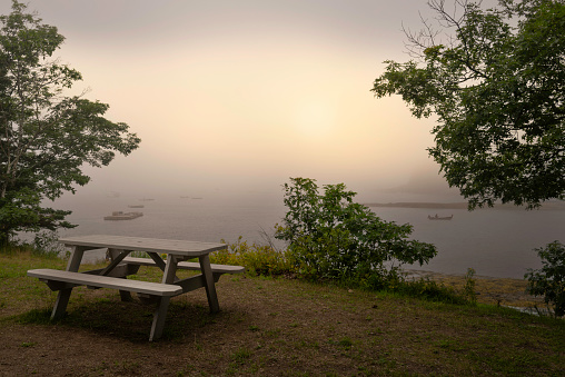 Foggy morning seascape with empty bench and table on the green hill at Boothbay Harbor in Lincoln County, Maine