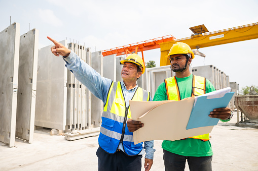 construction blueprint paper. Asian indian construction architect Engineering man and senior worker in safety hardhat working on blue print at Prefabricated concrete factory Heavy industrial