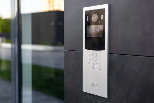 Entrance doorbell in a multi-apartment building, with a video surveillance camera, on a dark wall.