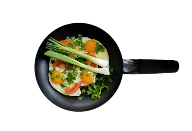 Fried eggs with green onions in a frying pan isolated on white background