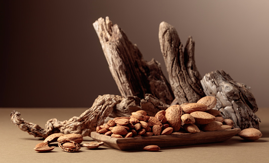 Almond nuts in a wooden dish on a brown background. Still life with fresh-cropped nuts and old snags.
