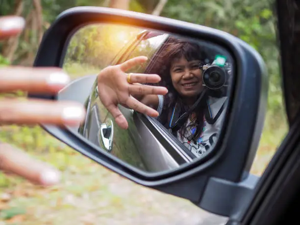 Photo of A woman holds a digital camera and takes a picture of herself smiling reflected in the car mirror.