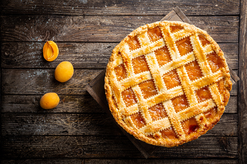 Summer apricot or peach pie homemade on wooden background, top view. Delicious fruit dessert. Fruit cake. Copy space.