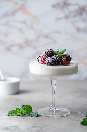 Delicious italian dessert panna cotta with iced berries and mint on light background.