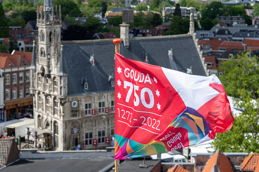Gouda, The Netherlands-June 2022; Close up view of flag with design and color celebrating Gouda received city rights 750 years ago; historic market square and city hall out of focus as background
