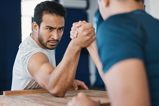 Strength, motivation and male people arm wrestling on a table while being playful for a challenge. Rivalry, game and men athletes doing strength muscles battle for fun, bonding and friendship in gym.