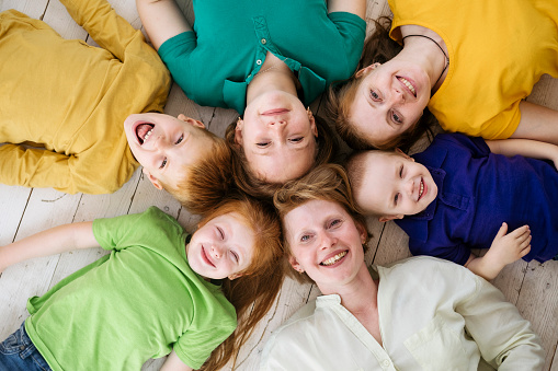 Two red-haired sisters and their children are lying on the floor and laughing merrily. Red-haired women and their offspring. Two generations together, human relationships.