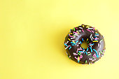 glazed chocolate donut with colorful sugar sprinkles isolated on yellow background