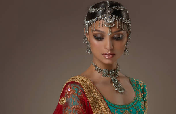 Model dressed in a traditional Indian suit-sari and bright silver jewelry. Indian beauty. Young attractive woman dressed in a traditional Indian suit-sari, with green blouse and red shawl (dupatta) with gilded decoration. Her head, ears and neck is decorated by flamboyant silver jewelry. asian eyebrows stock pictures, royalty-free photos & images
