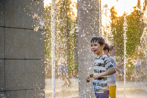 Boys jumping in water fountains. Children playing with a city fountain on hot summer day. Happy friends having fun in fountain. Summer weather. Friendship, lifestyle and vacation.