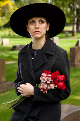 Sad Woman grieves in a cemetery, holding roses and lilies.
