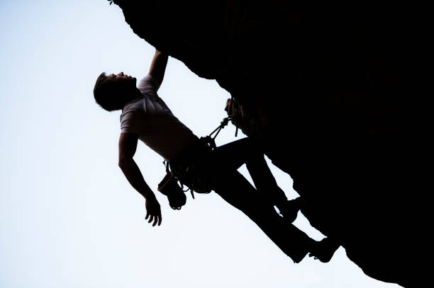 An adaptive climbing student pauses midway through an ascent, gripping the rope system while catching their breath before continuing. The image captures the tension, control, and quiet determination in moments of physical challenge—highlighting resilience, self-awareness, and strategic recovery in sport.