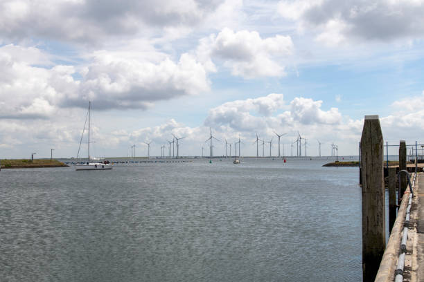 Bruinisse, the Netherlands-June 2022; Panoramic view over the harbour of Bruinisse with some sailships in front and large wind turbine farm in the background