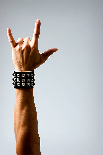 Man in Wristband making Rock & Roll Hand Symbol close up of Man with studded wristband making rock symbol. Studio photo with Dramatic lighting, slight vignette for effect. hand gestures stock pictures, royalty-free photos & images