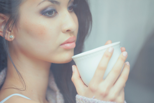 young woman sitting in the window on a melancholic day with a cup of hot tea