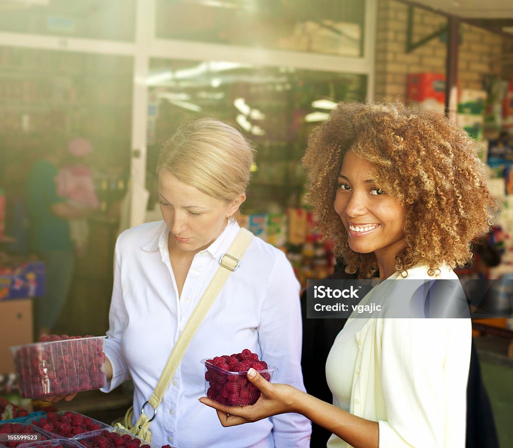 Women at market buying raspberry. Two woman, african american and Caucasian, friends shopping at a open market, buying fruits, raspberry. Open Market in Belgrade, Serbia, Europe. Fruit Stock Photo
