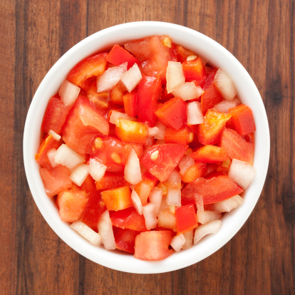 Top view of white bowl full of salad composed of diced tomato, red pepper and onion