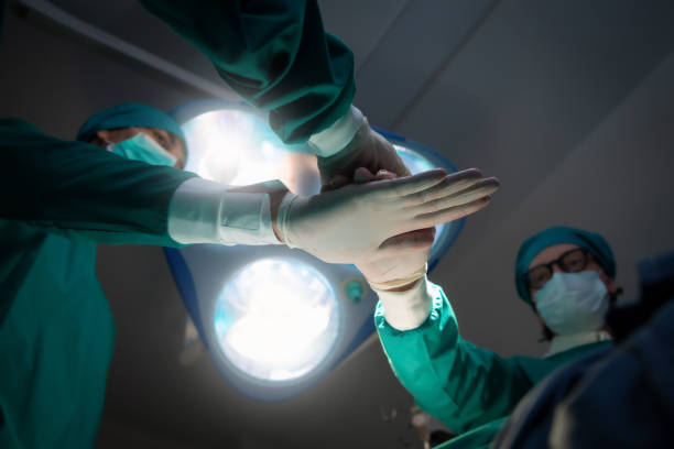 istock Doctors and team performing coordinate hands in bright Modern operating room with lighting equipment at hospital. Concept Teamwork in hospital for success work and trust in team 1555999934