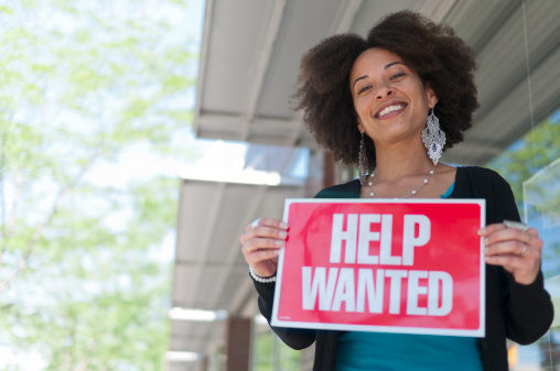 Business woman holding help wanted sign up outside of a store front. Photograph taken in Grand Rapids, Michigan.