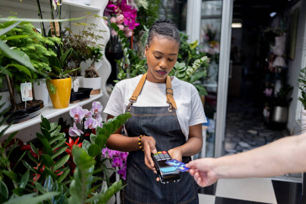istock Female florist Black ethnicity holding POS terminal, while customer paying purchase with credit card 1556006159