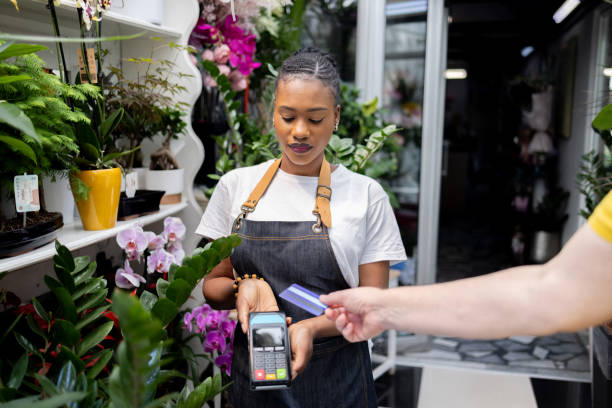 istock Female florist Black ethnicity holding POS terminal, while customer paying purchase with credit card 1556007235